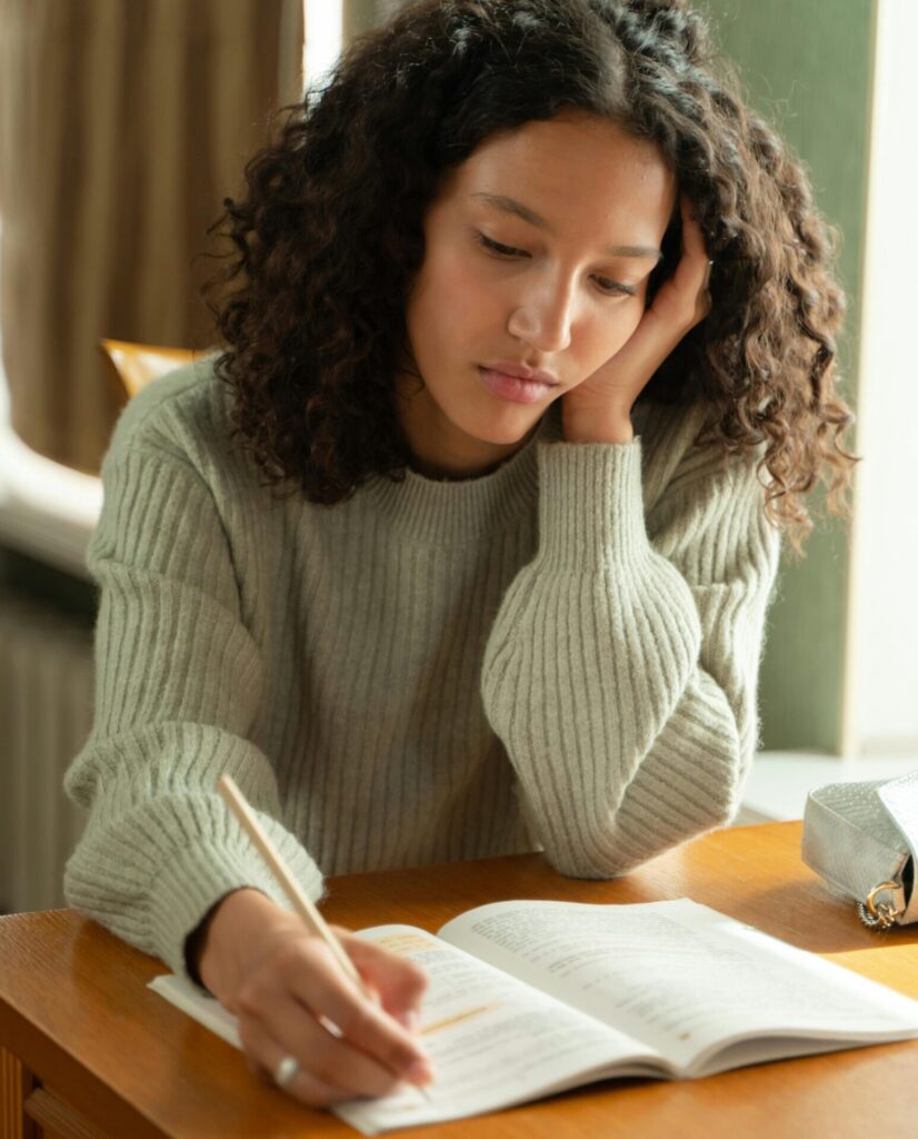 Teenage girl with curly hair studying at a desk, concentrated on her homework.